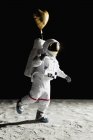 Astronauta caminando en la luna y sosteniendo el globo de helio en forma de corazón - foto de stock