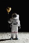 Astronauta en la superficie de la luna sosteniendo globo de helio en forma de corazón - foto de stock