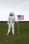 Astronauta de pie en el césped y posando con bandera americana - foto de stock