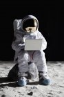 Astronauta sentado en la roca en la luna y usando el ordenador portátil - foto de stock