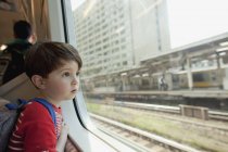 Цікаво хлопчик дивлячись через скляне вікно під час подорожі в поїзді — стокове фото