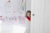 Portrait of cheerful girl hiding behind door against drawing on wall — Stock Photo