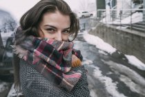Retrato mujer joven confiada en bufanda a cuadros en la calle nevada de invierno - foto de stock