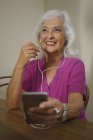 Mujer mayor sonriente escuchando música con auriculares y reproductor de mp3 — Stock Photo