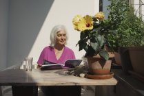 Старшая женщина читает журнал на солнечном патио — стоковое фото