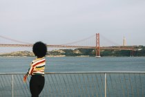 Giovane donna in piedi sul lungomare, guardando 25 de Abril Bridge e Cristo Rei Statua, Lisbona — Foto stock