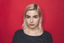 Retrato de mujer con cabello blanqueado y expresión seria sobre fondo rojo - foto de stock
