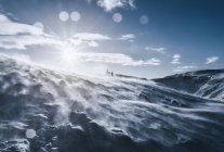 People walking along sunny, windy, snow covered mountain, Reykjadalur, Iceland — Stock Photo