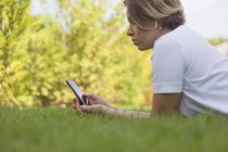 Mujer joven con auriculares usando teléfono inteligente en la hierba - foto de stock
