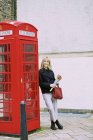 Frau mit Tulpenstrauß lehnt an roter Telefonzelle — Stockfoto