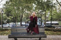Donna spensierata che ascolta musica con le cuffie sulla panchina del parco urbano — Foto stock
