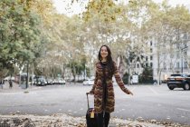 Retrato de mujer turista feliz con maleta en calle urbana otoñal - foto de stock