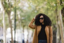 Élégante jeune femme en lunettes de soleil marchant dans le parc — Photo de stock