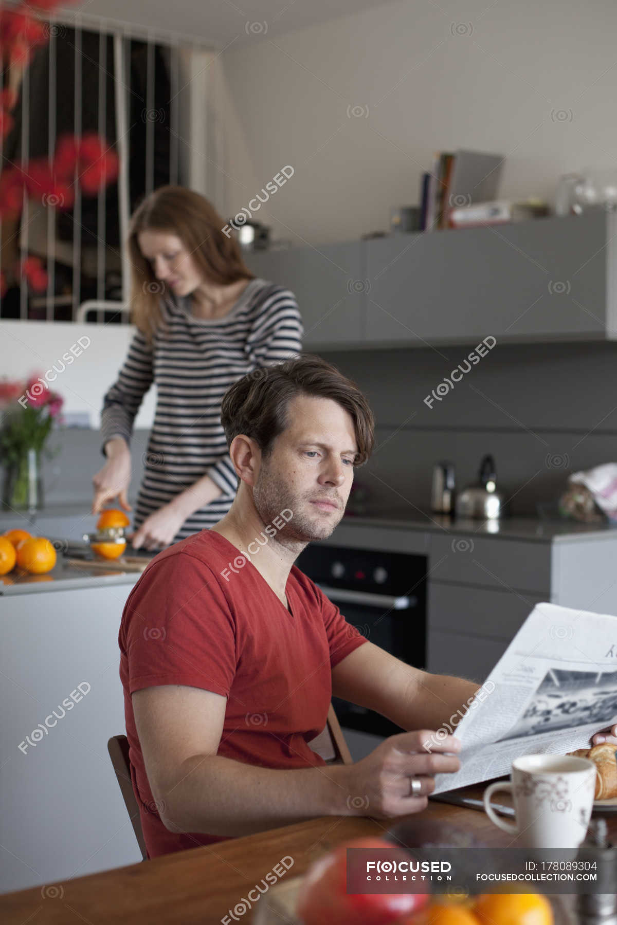 Man Reading Newspaper In Kitchen While Woman Making Orange Juice On Background Male Fruit Stock Photo