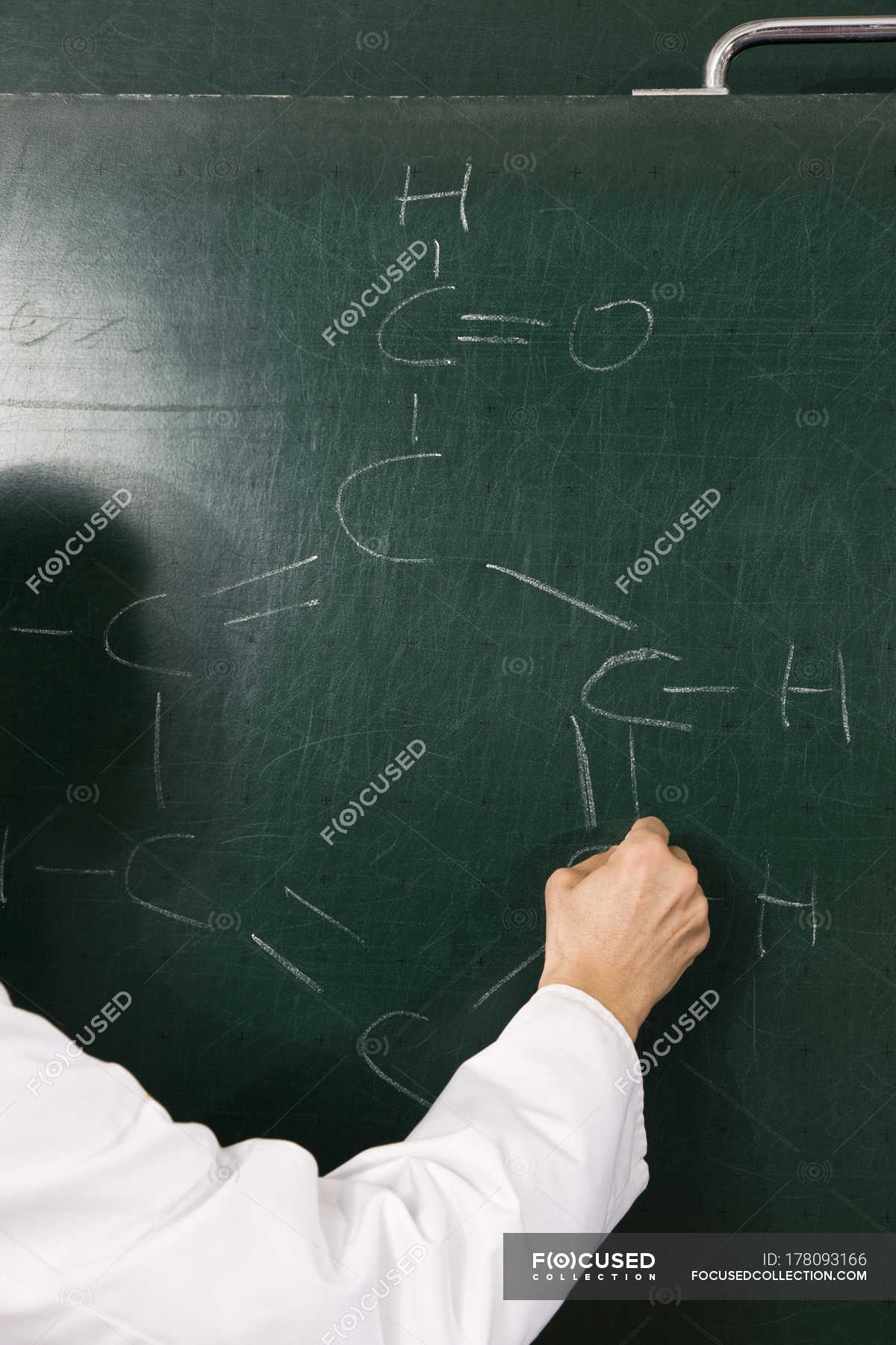 A chemistry teacher writing a formula on a chalkboard, focus on hand