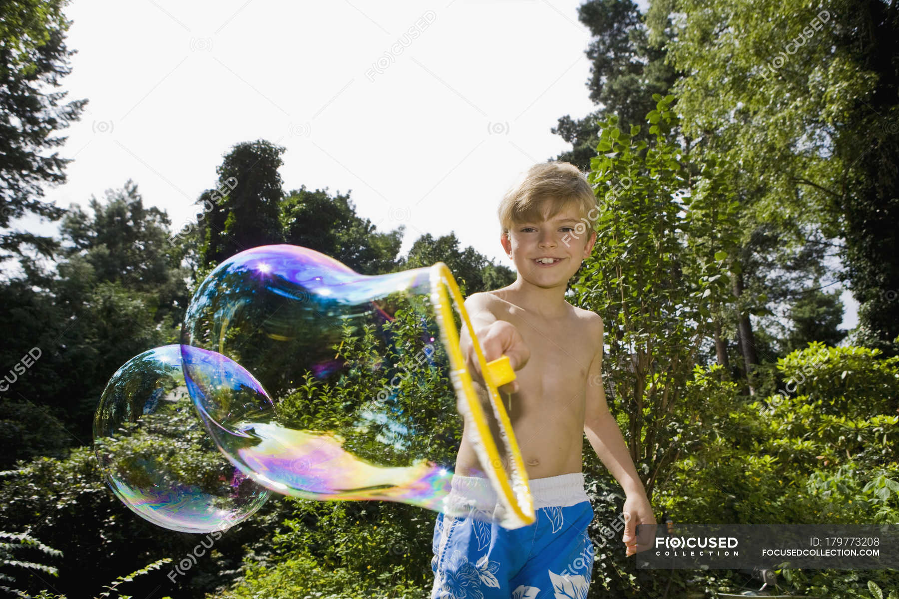 Boy Making A Bubble With A Bubble Wand In Garden Looking At