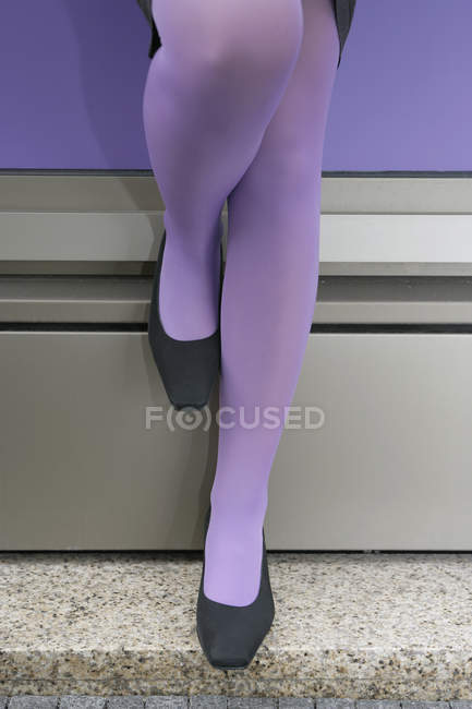 Нижняя часть женщины в фиолетовых колготках опирается на стену — стоковое фото