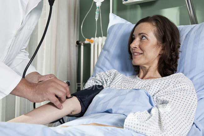 Un hombre que revisa la presión arterial de una paciente femenina - foto de stock