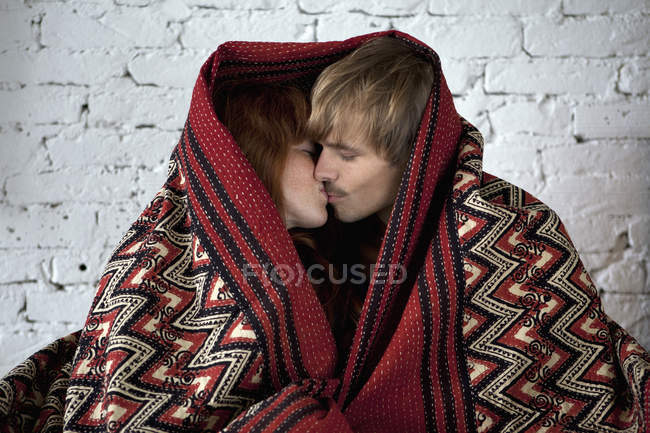Un jeune couple enveloppé dans une couverture embrasser — Photo de stock