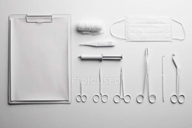 Clipboard by medical scissors and various instruments painted white and arranged neatly — Stock Photo