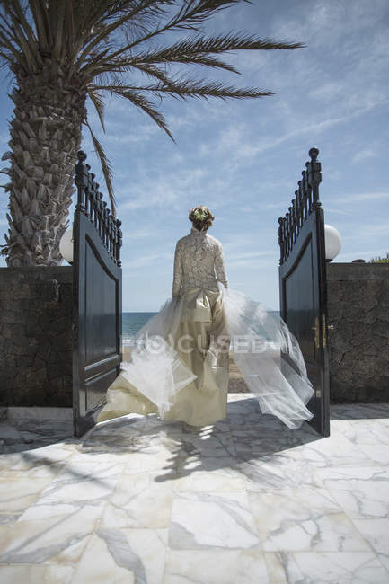 Вид сзади невесты, идущей через ворота к пляжу — стоковое фото