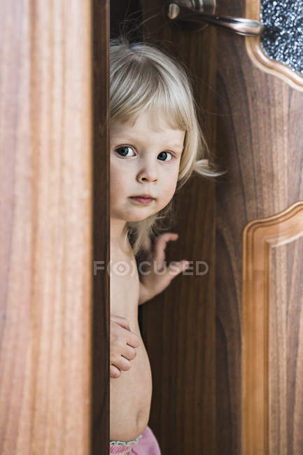 Blonde Little Girl Standing By Open Door And Looking At Camera