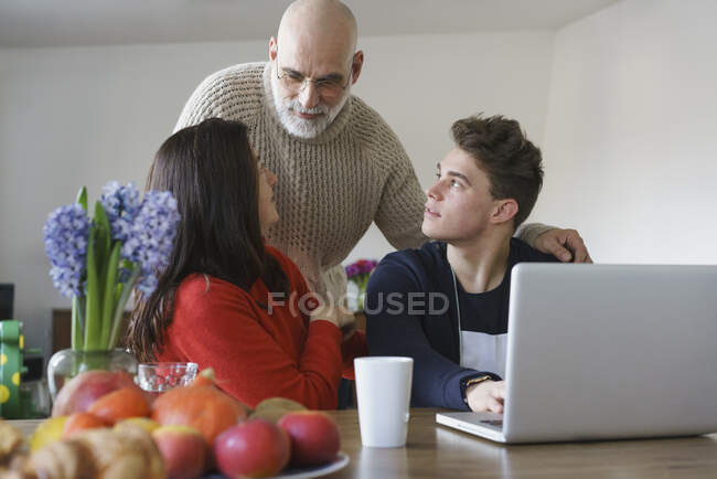 Familia hablando por mesa con el ordenador portátil en casa - foto de stock