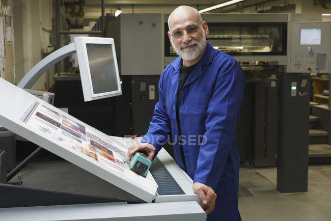 Portrait of smiling mature worker standing by equipment at printing press — Stock Photo