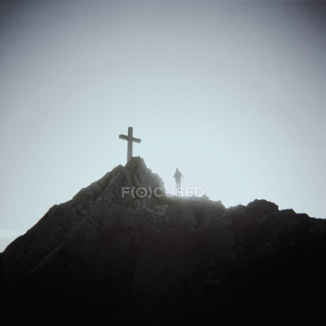 Persona silueta de pie debajo del crucifijo en la cima de la montaña
, - foto de stock