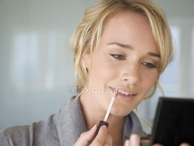 Una joven aplicando brillo labial - foto de stock