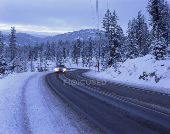 Размытый автомобиль на снежной горной дороге в сумерках — стоковое фото