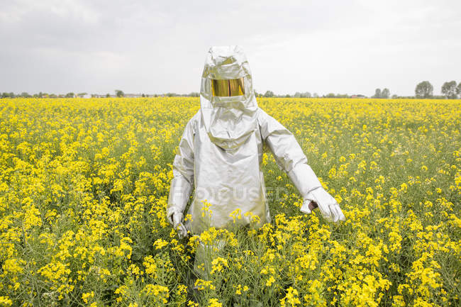 Persona in tuta protettiva contro le radiazioni in piedi nel campo di colza — Foto stock
