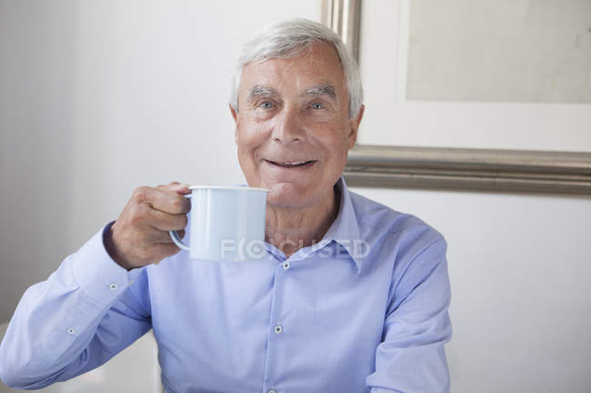 Ritratto di uomo anziano felice che tiene una tazza di caffè a casa — Foto stock