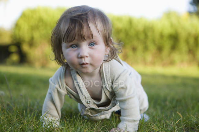 Bébé fille rampant dans l'herbe et regardant la caméra — Photo de stock