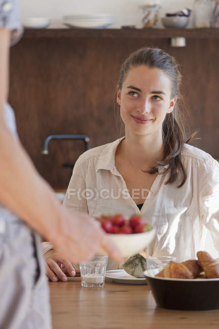 Smiling young woman sitting at dining table with breakfast — Stock Photo