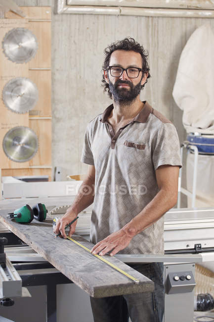 Portrait of male carpenter measuring wood in workshop — Stock Photo
