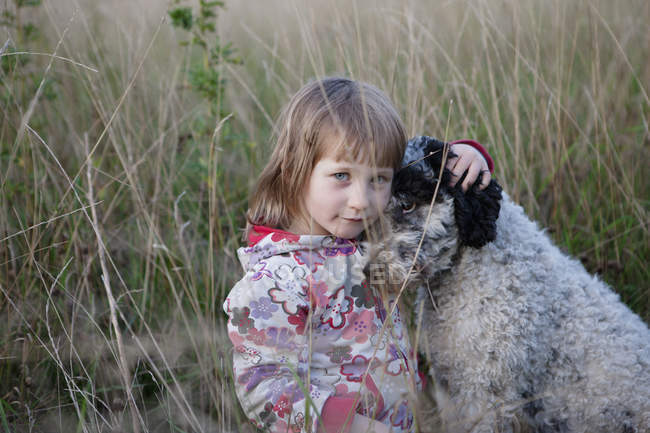 Porträt eines süßen Mädchens, das mit Hund auf dem Feld sitzt — Stockfoto