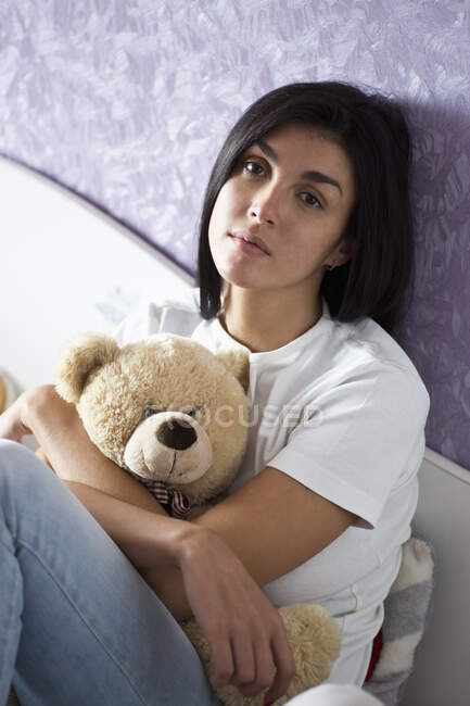 Mujer abrazando osito de peluche en la cama - foto de stock