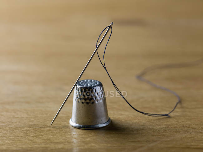 Threaded needle balanced against shiny metal thimble — Stock Photo