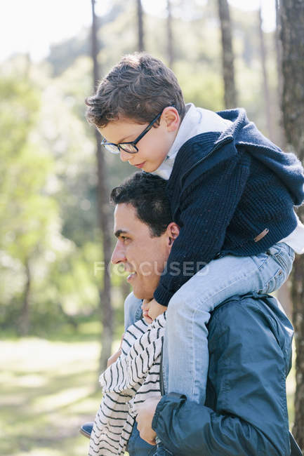 Uomo sorridente che porta il figlio sulle spalle nella foresta — Foto stock