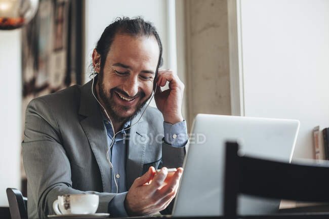 Счастливый бизнесмен средних лет слушает музыку через мобильный телефон в кафе — стоковое фото