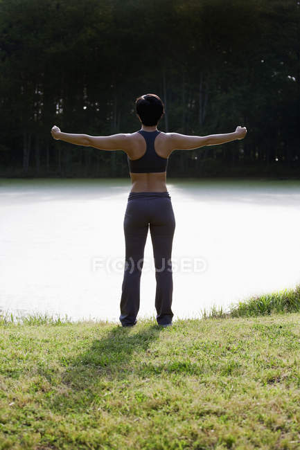 Задній вид жінка розтягування зброї на Туманний озера — стокове фото