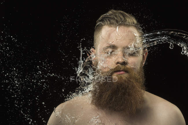 Agua salpicando en la cara del hombre contra el fondo negro - foto de stock