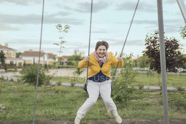 Щасливі старший жінка гойдаються на гойдалки на майданчику проти неба — стокове фото