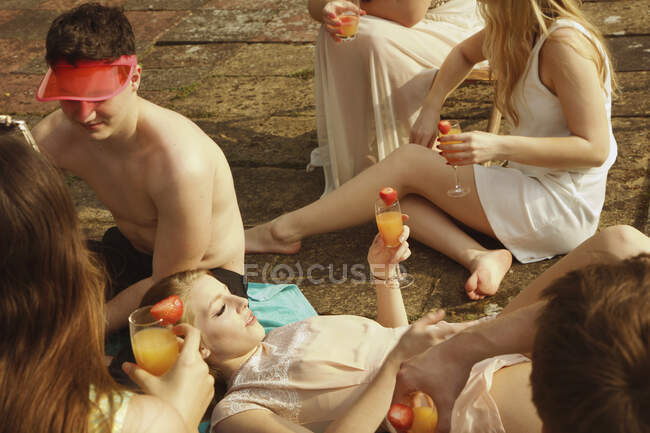 Vista de ángulo alto de amigos sosteniendo bebidas mientras se relajan junto a la piscina - foto de stock