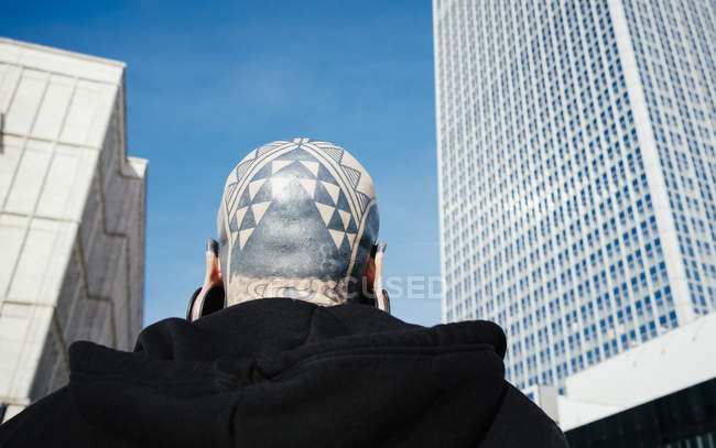 Rear view of man with tattoos and ear plugs against skyscraper — Stock Photo