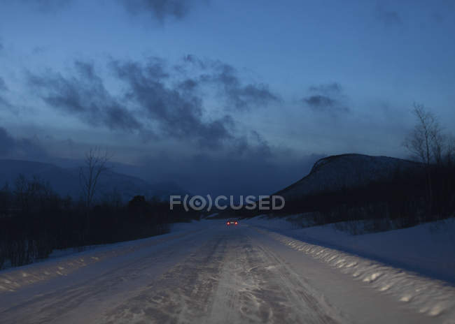 Distante visão traseira do carro andando na neve estrada coberta ao entardecer — Fotografia de Stock
