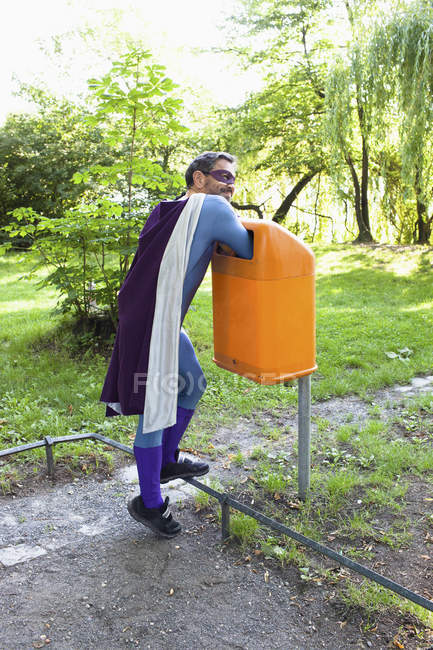 Mature male superhero putting hands in orange garbage bin — Stock Photo