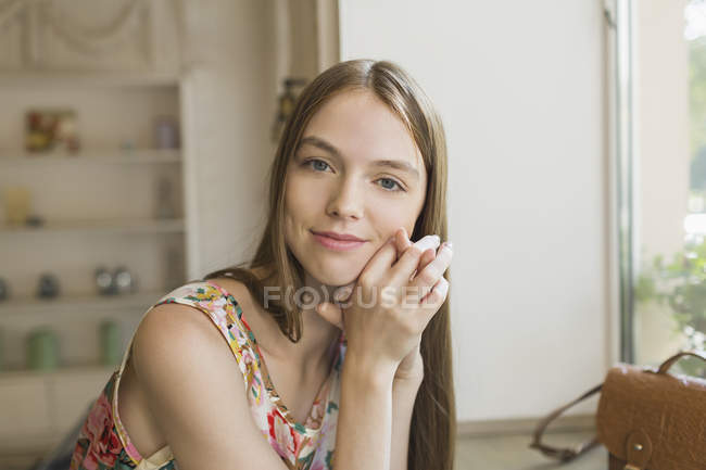 Retrato de una hermosa mujer sonriente apoyada en la mesa por la ventana - foto de stock