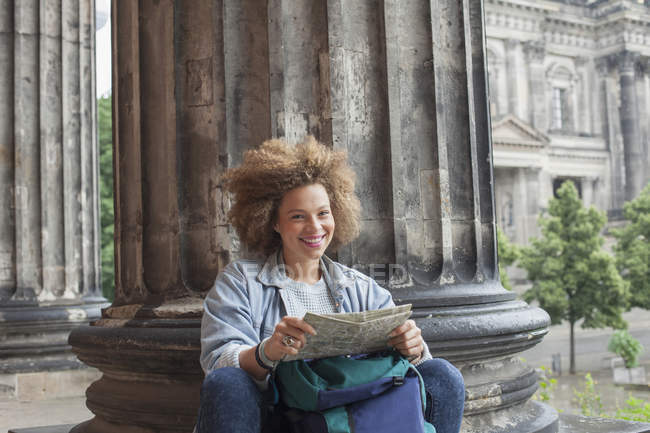 Portrait de jeune touriste afro souriante assise avec carte contre colonne au Musée Altes — Photo de stock